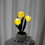 a white vase with yellow flowers on top of a stack of books