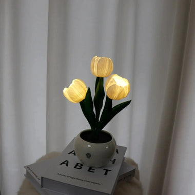 three orange tulips in a white vase on top of a stack of books