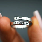 a person holding two silver rings that say i am enough